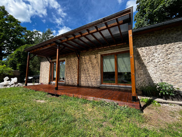 Stone house with a wooden deck and pergola under a blue sky.