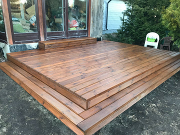 Wooden deck construction with a house and garden in the background