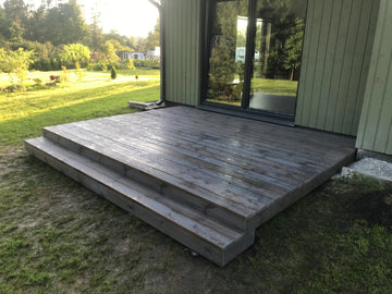 Wooden deck with steps leading up to a house with large windows.