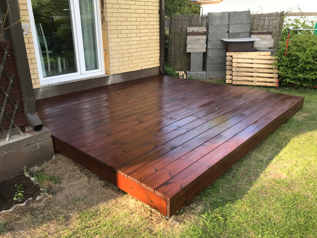 Wooden deck extending from a house with grass and building materials in the background
