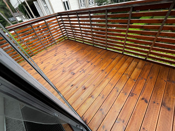 Wooden deck on balcony with railing and greenery in the background