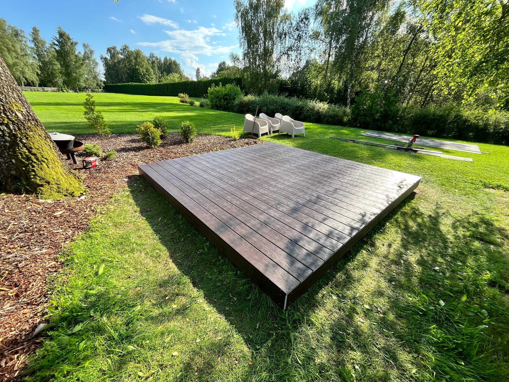 Wooden platform in a garden with trees and grass in the background