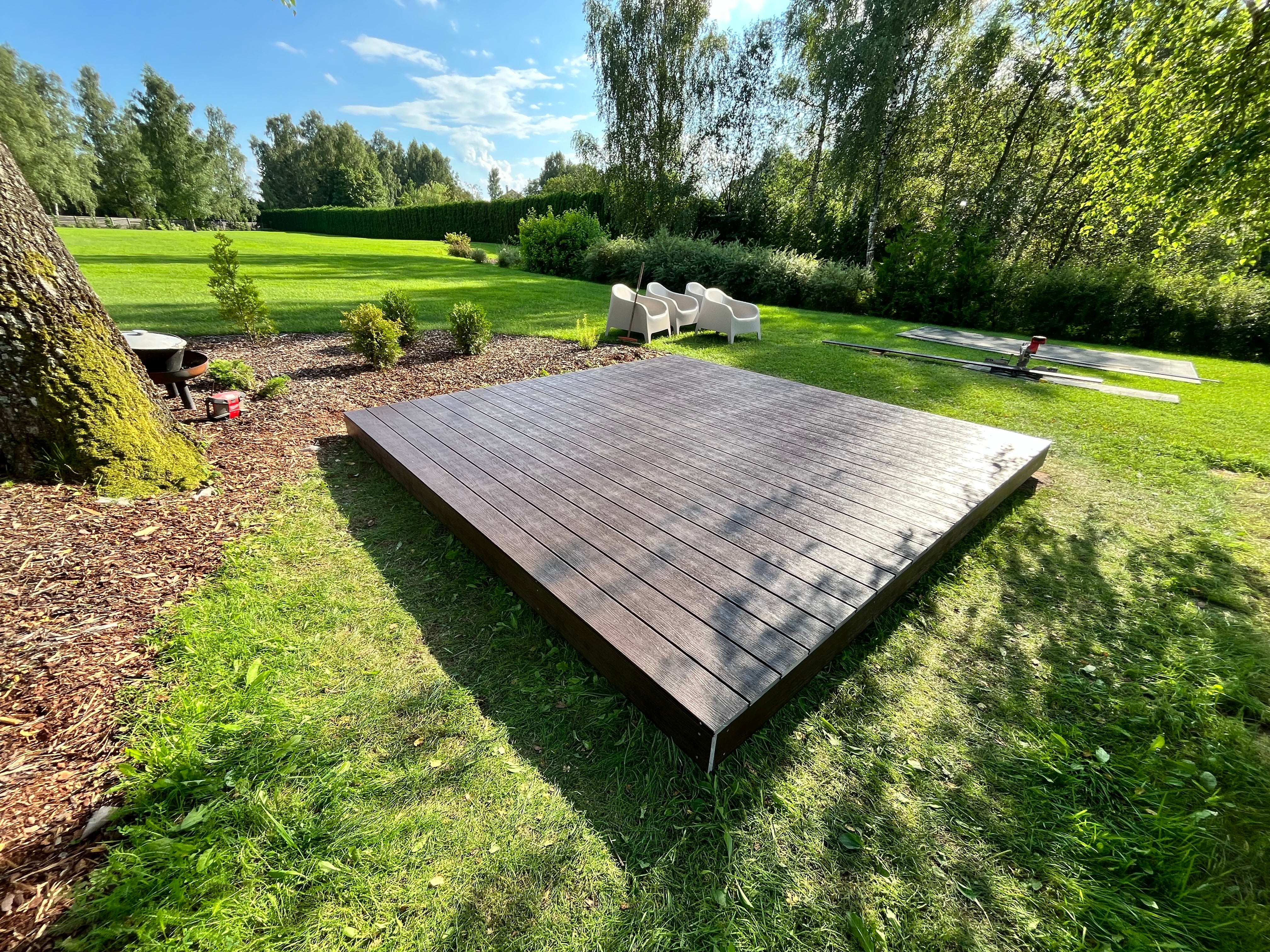 Wooden platform in a garden with trees and grass in the background