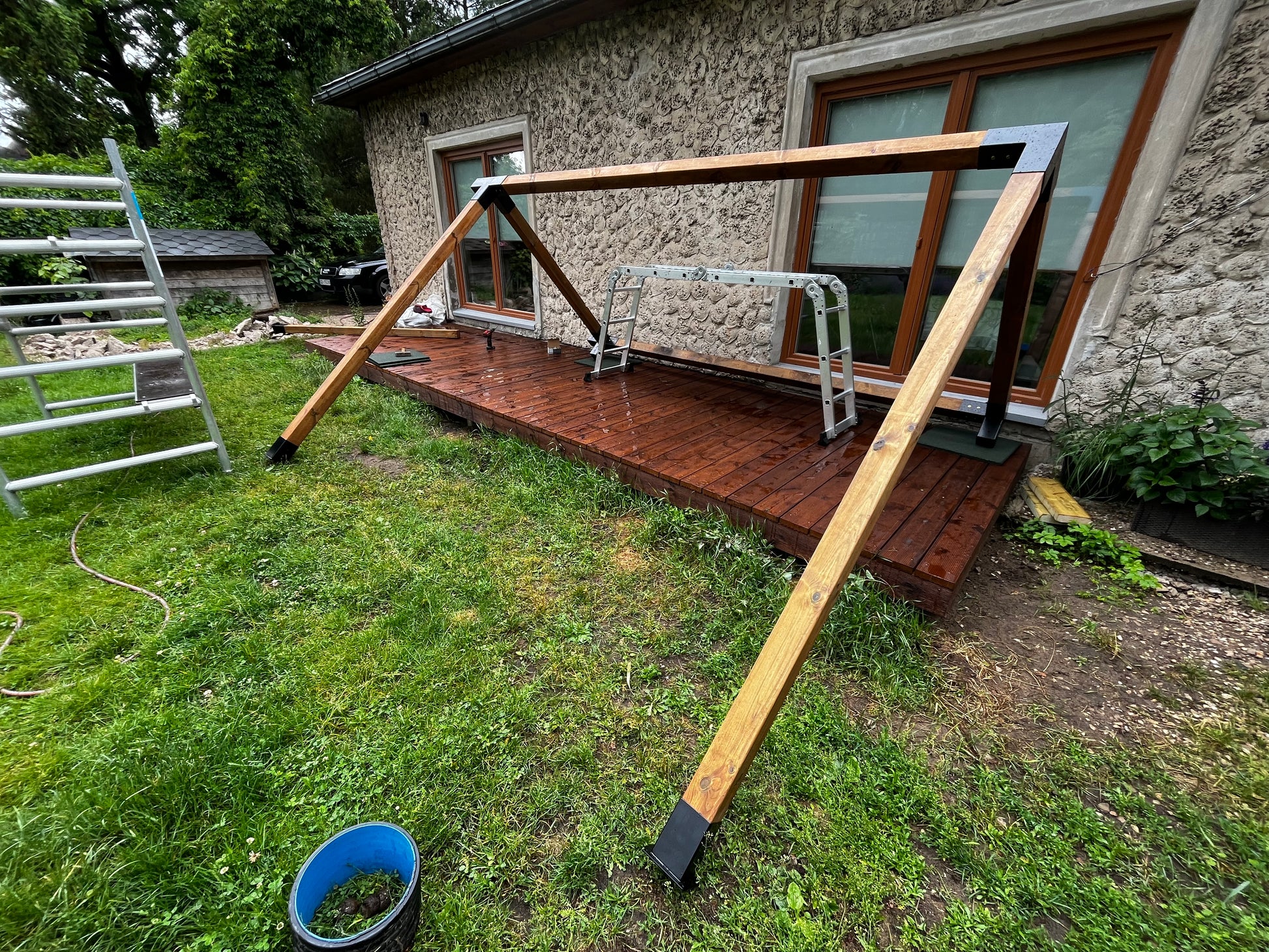 Wooden swing set on a deck with a stone house in the background