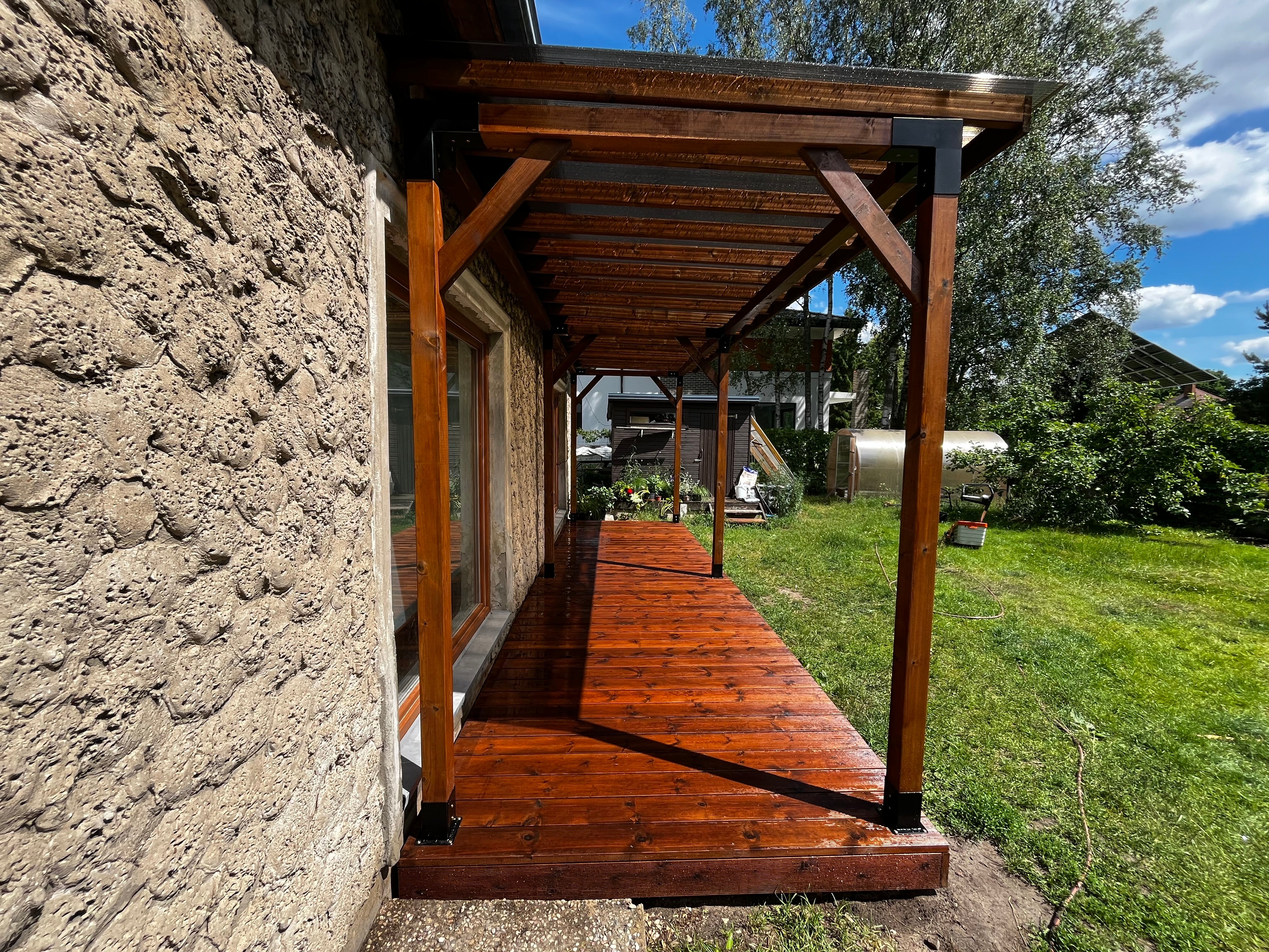 Wooden deck attached to a stone building with a garden and trees in the background.