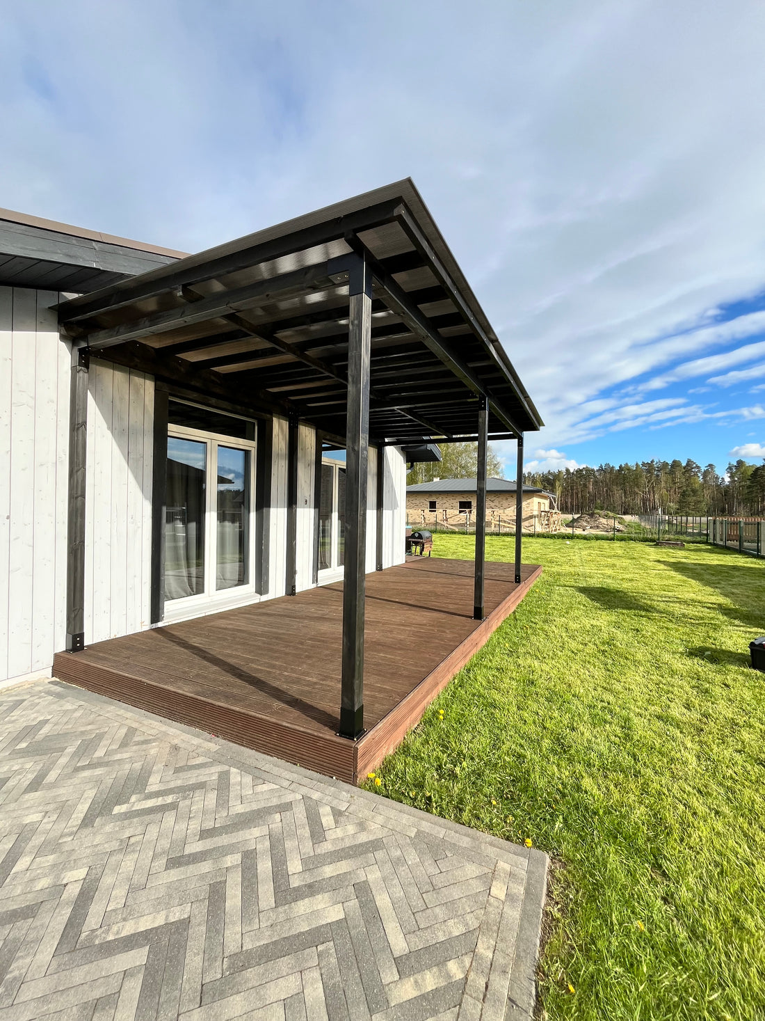 Modern house exterior with a deck, lawn, and car in the driveway under a blue sky.