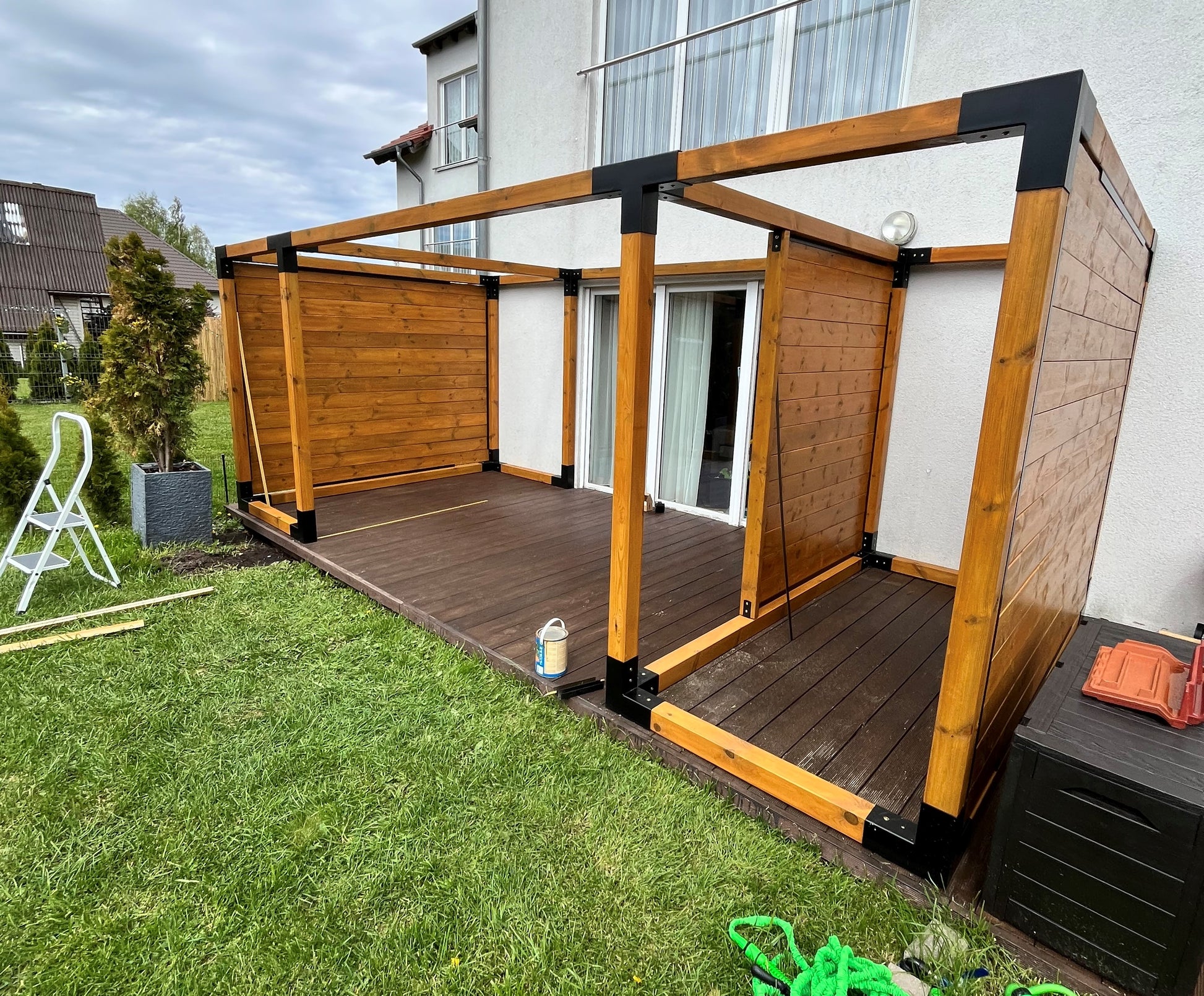 Wooden pergola structure on a grassy area with a house in the background