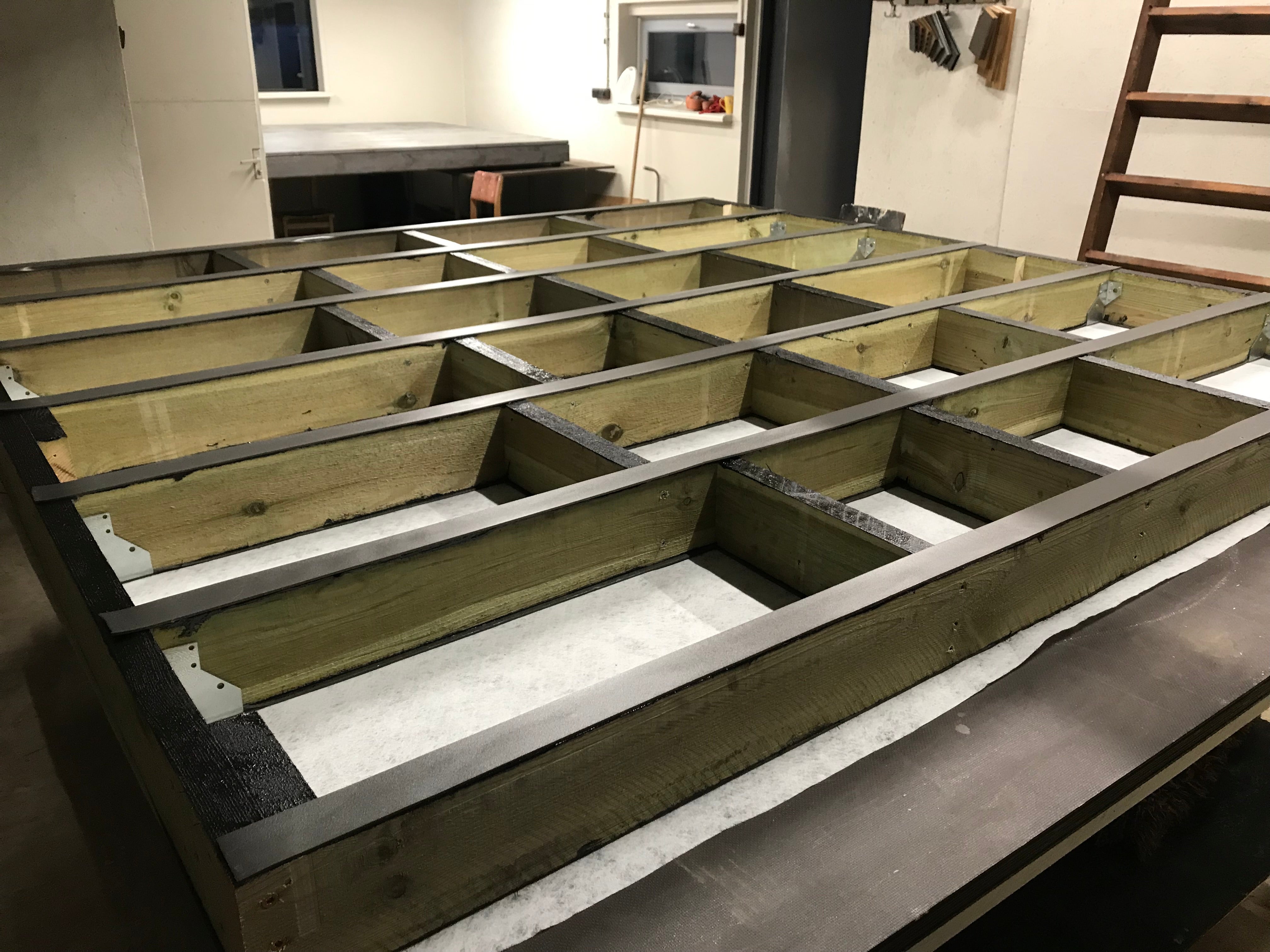 Wooden floor joists on a concrete floor with a kitchen in the background