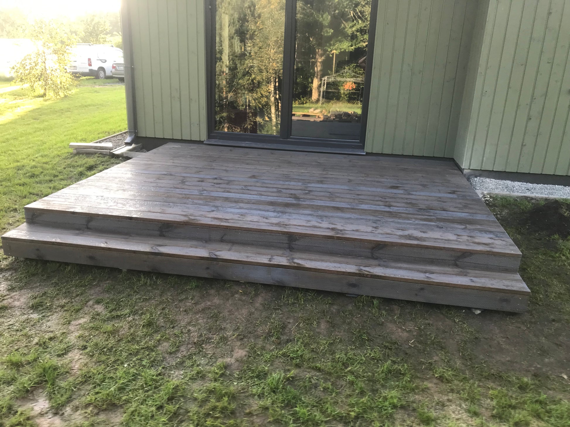 Wooden deck extending from a house with grass and trees in the background