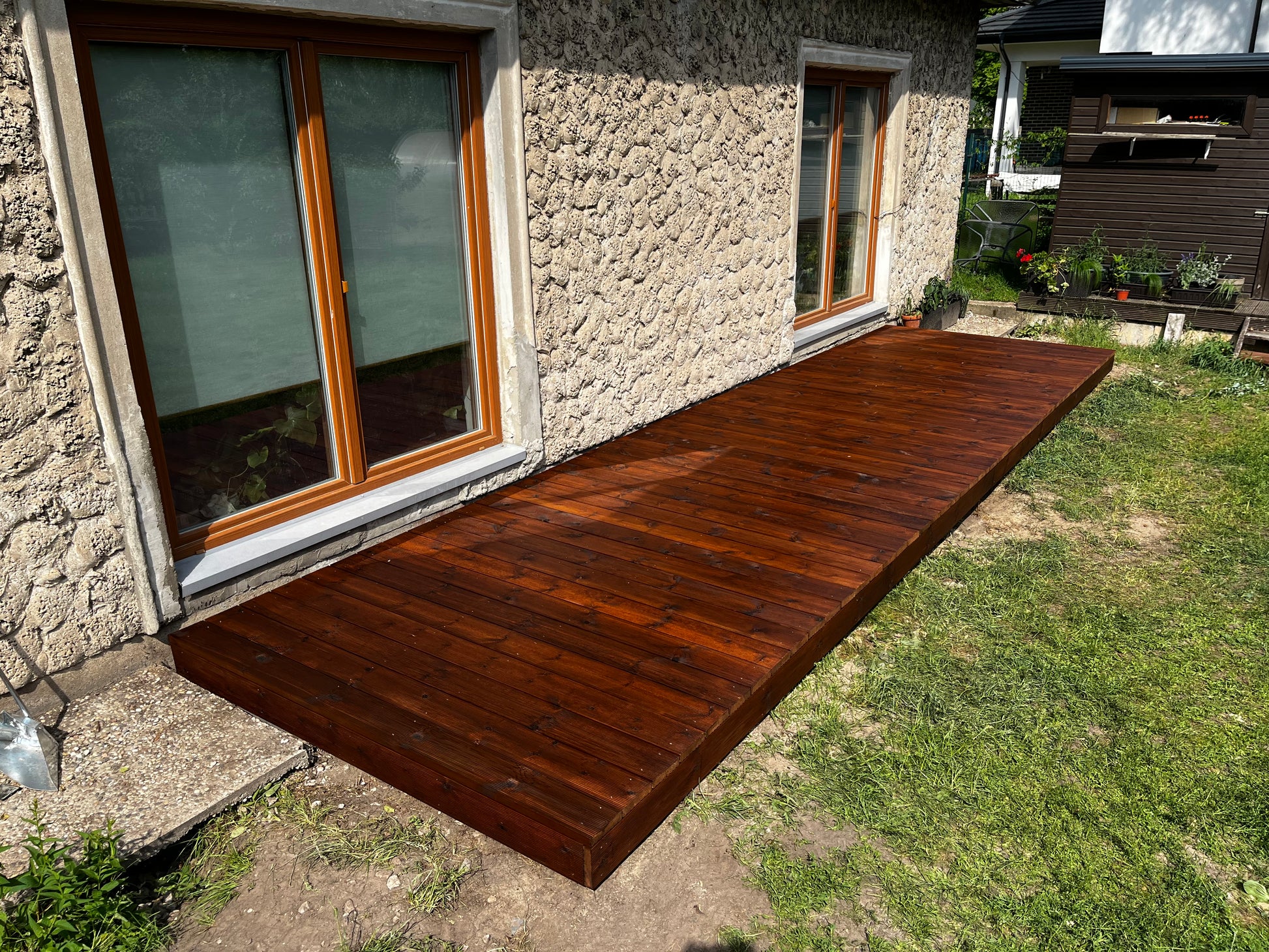 Wooden deck extending from a stone house with a garden in the background